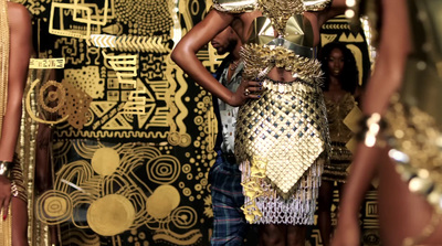 a woman standing in front of a wall covered in gold jewelry