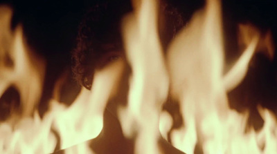 a woman standing in front of a fire filled wall