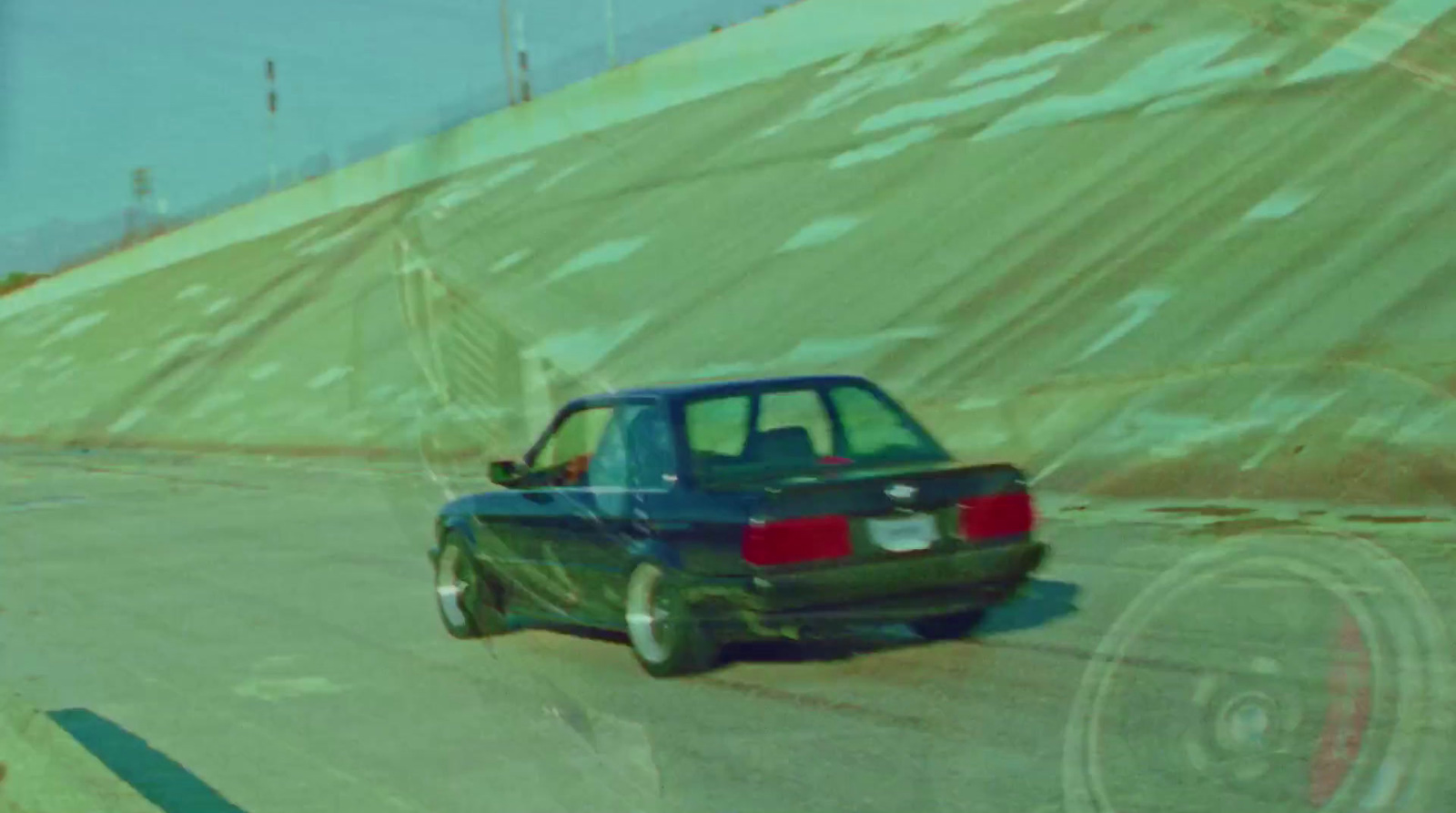 a green car driving down a road next to a hill