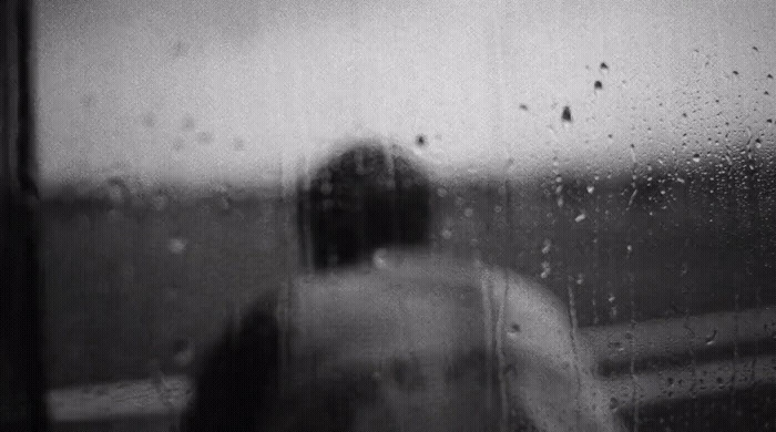 a black and white photo of a person looking out a window