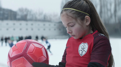 a young girl holding a soccer ball in the snow