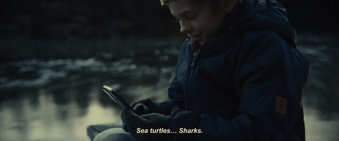 a young boy sitting on a rock looking at a cell phone