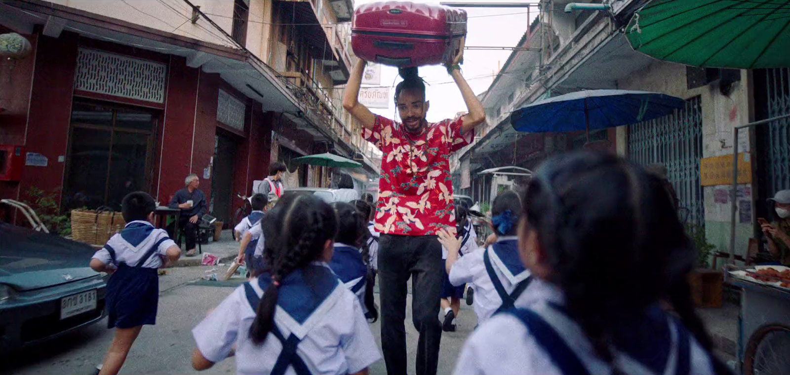 a man carrying a red object on his head down a street