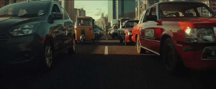 a group of cars driving down a street next to tall buildings