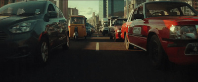 a group of cars driving down a street next to tall buildings