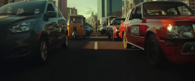 a group of cars driving down a street next to tall buildings