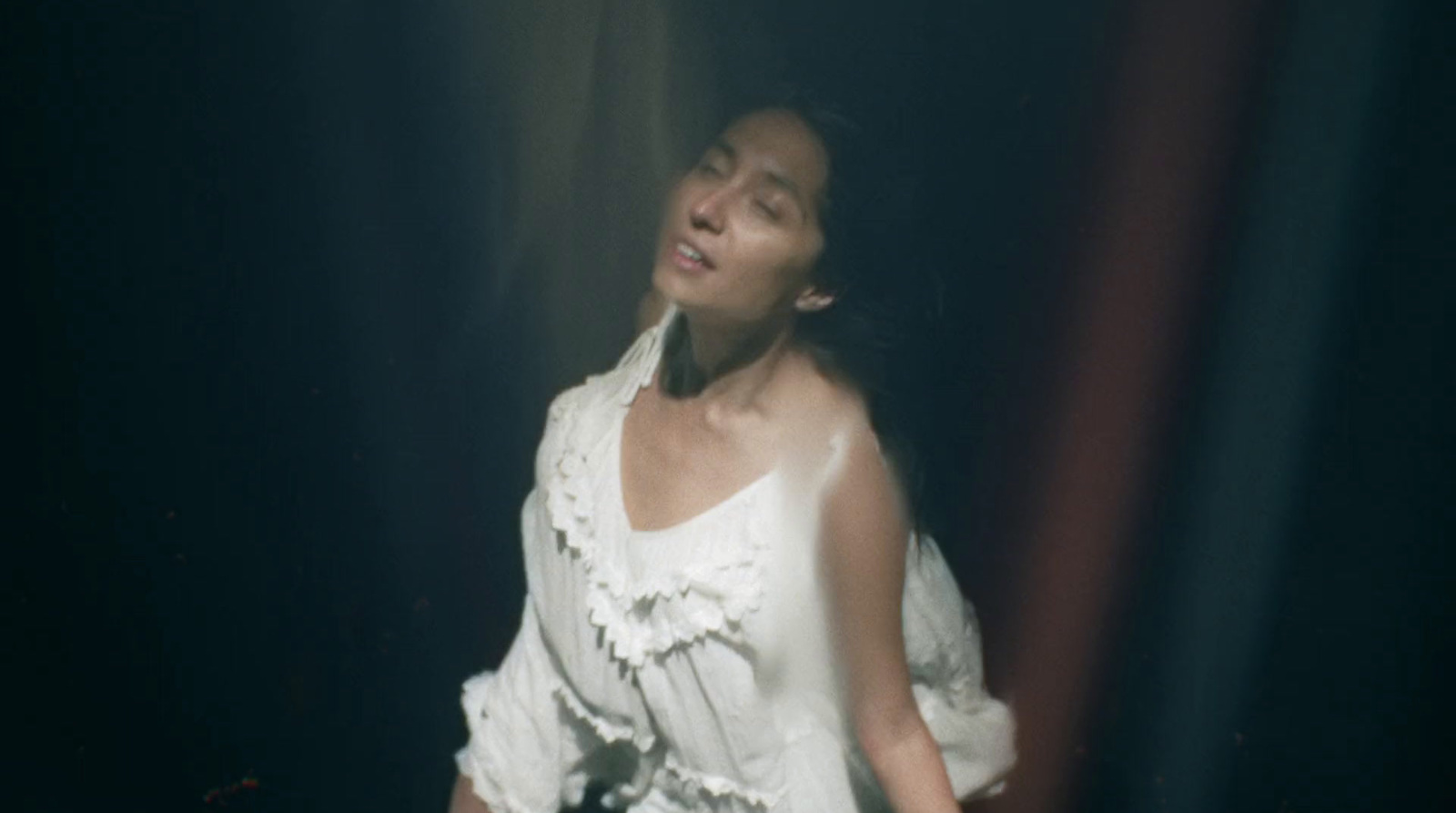 a woman in a white dress standing in a dark room