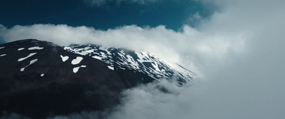 a mountain covered in snow and clouds under a blue sky