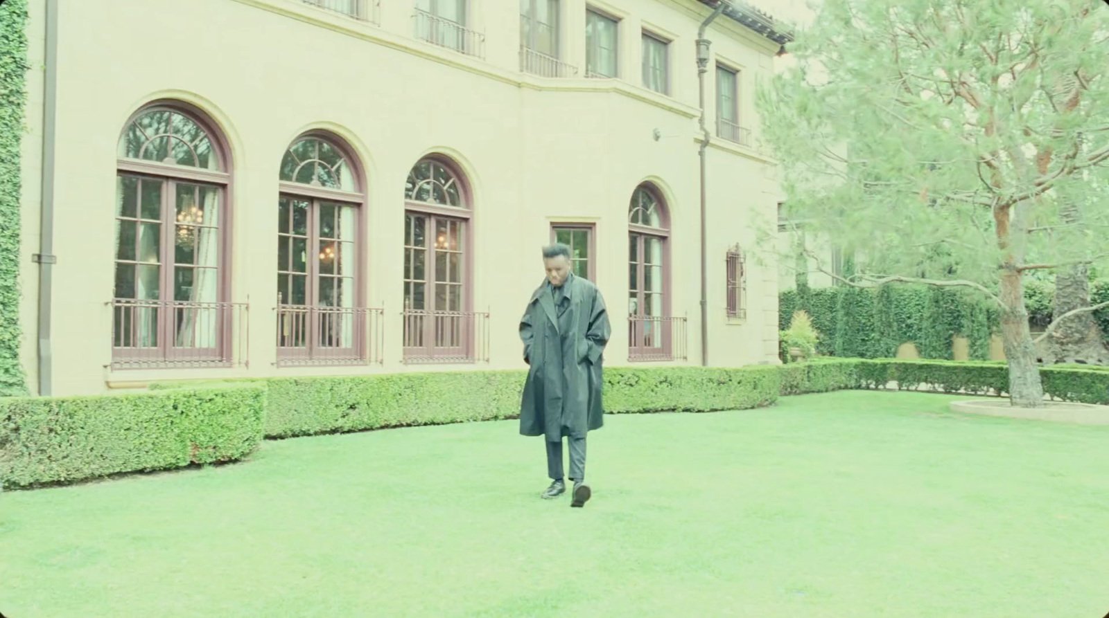 a man in a long coat walking in front of a building