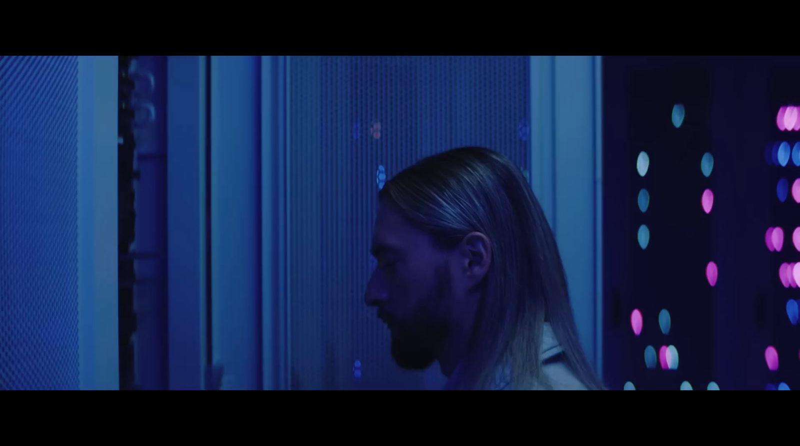 a man with long hair standing in a server room