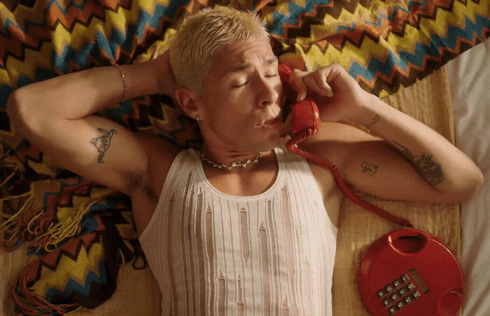 a man laying on a bed talking on a red telephone