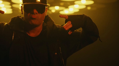 a man wearing a hat and sunglasses with his hands in the air