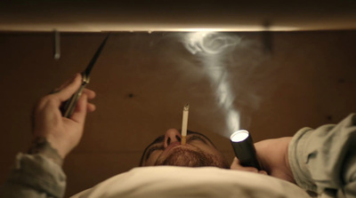 a man laying in bed with a lighter in his mouth