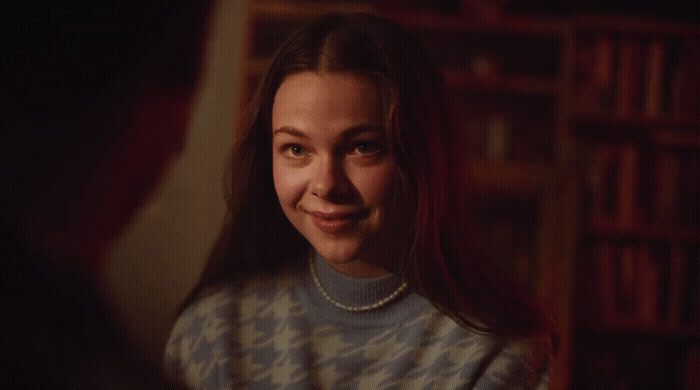 a woman with a pearl necklace smiling at someone