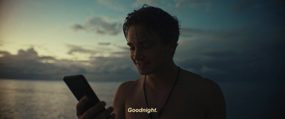 a man looking at his cell phone in front of the ocean