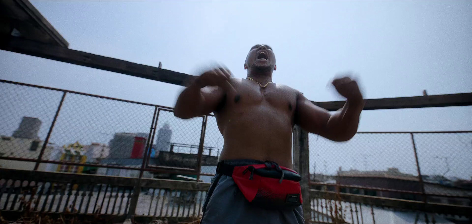 a shirtless man standing in front of a fence