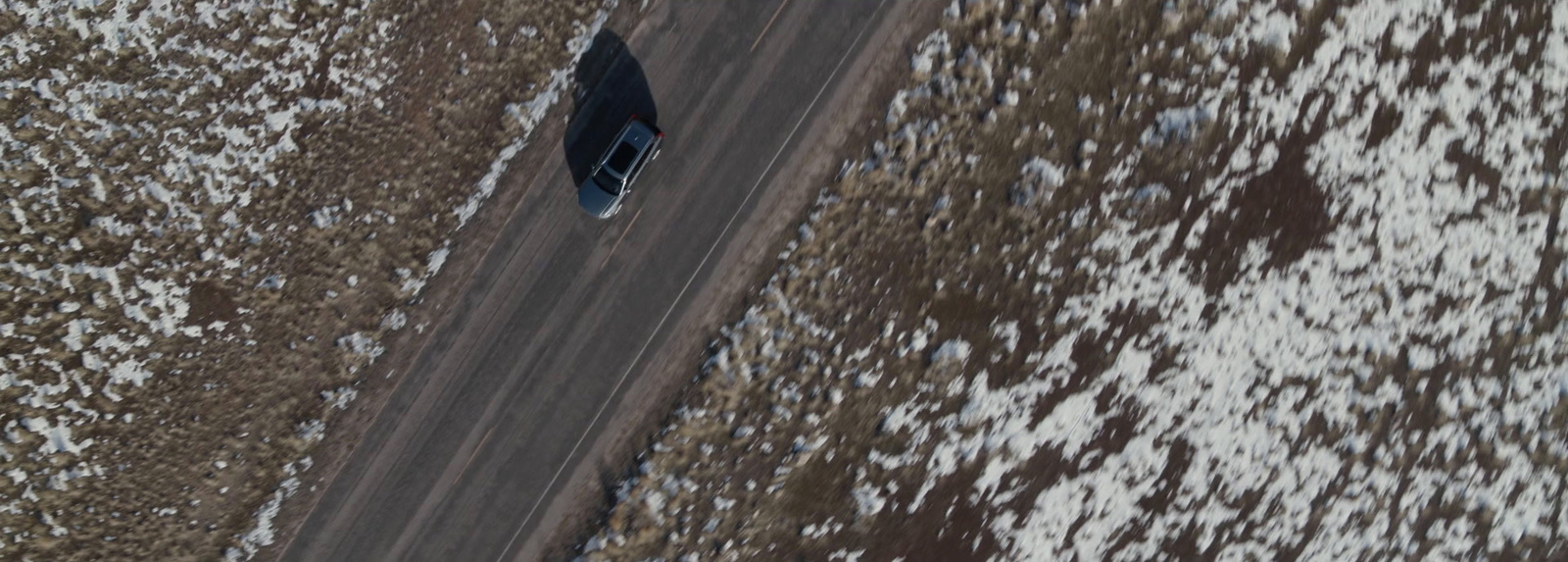 an aerial view of a car driving down a snowy road