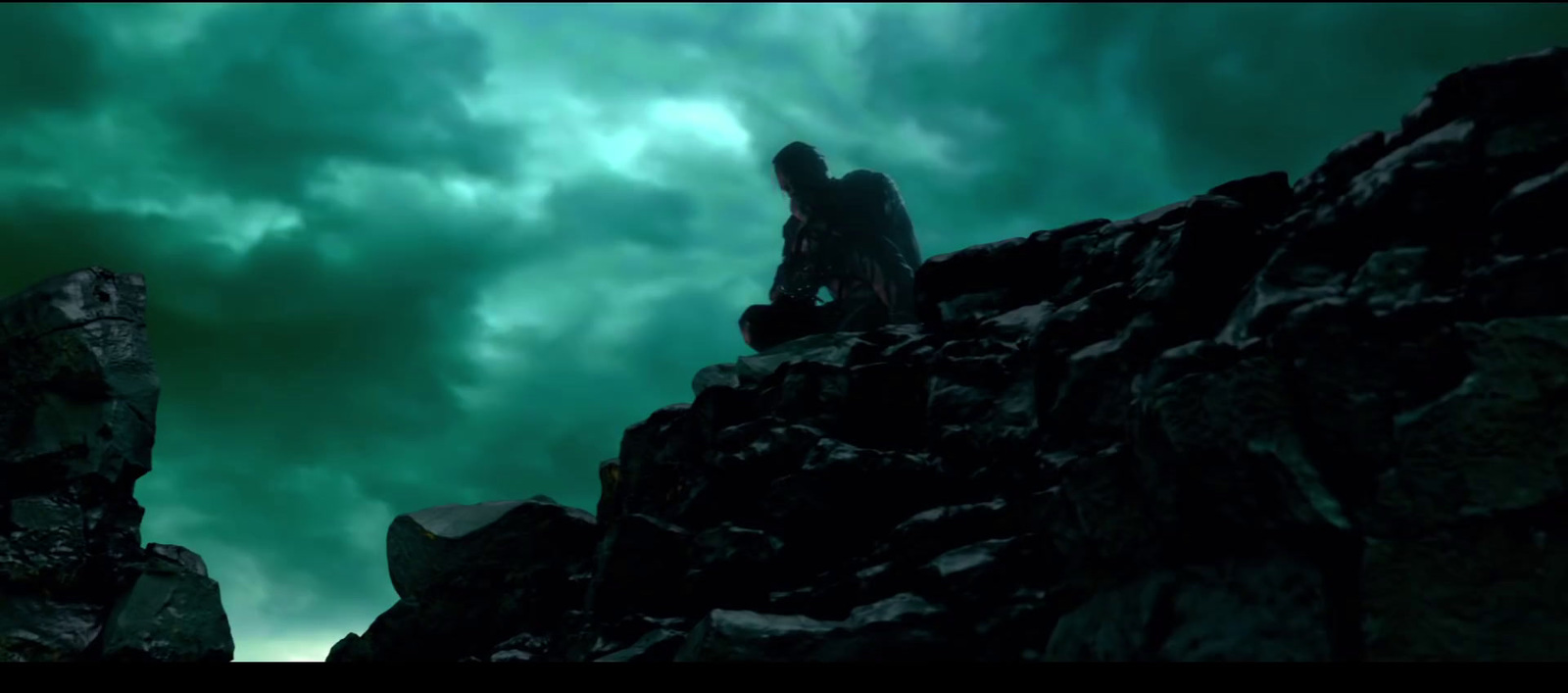 a man standing on top of a rocky cliff under a cloudy sky