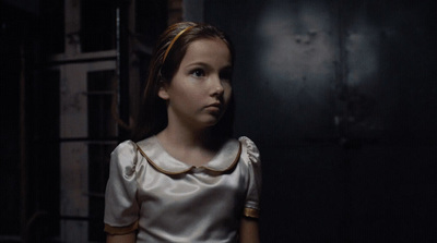 a young girl in a white dress standing in a dark room