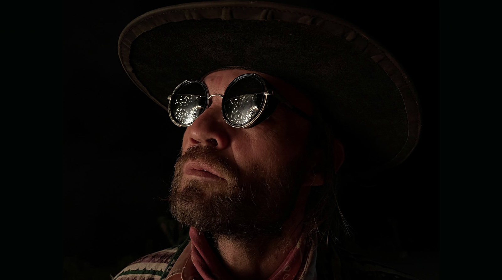 a man wearing a hat and sunglasses in the dark