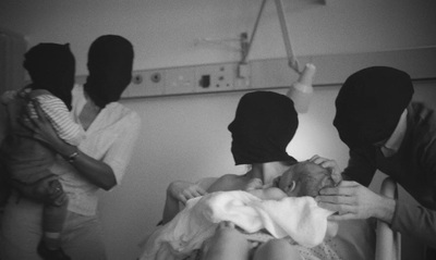 a group of people standing around a baby in a hospital bed