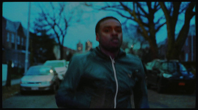 a man walking down a street next to parked cars