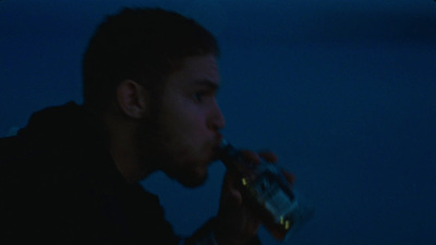 a man drinking from a bottle in a dark room