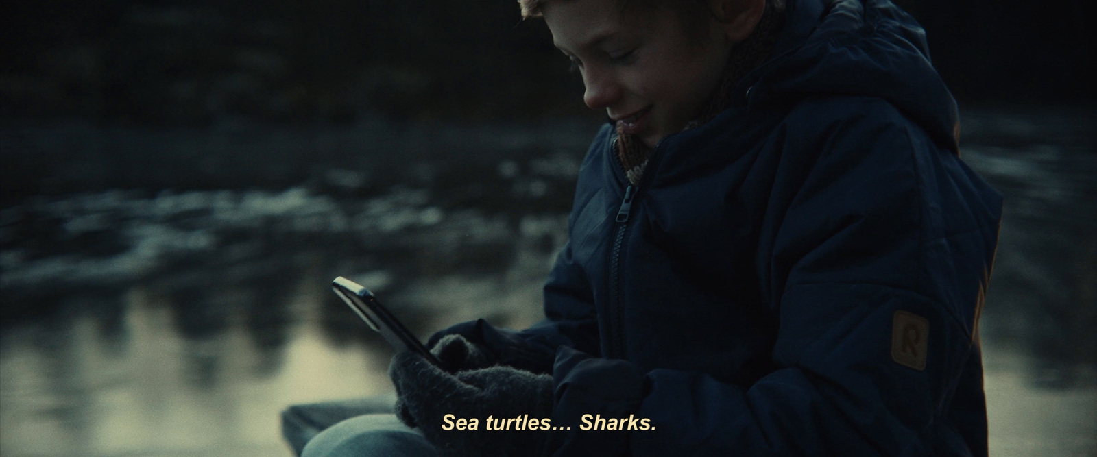 a young boy sitting on a bench looking at a cell phone