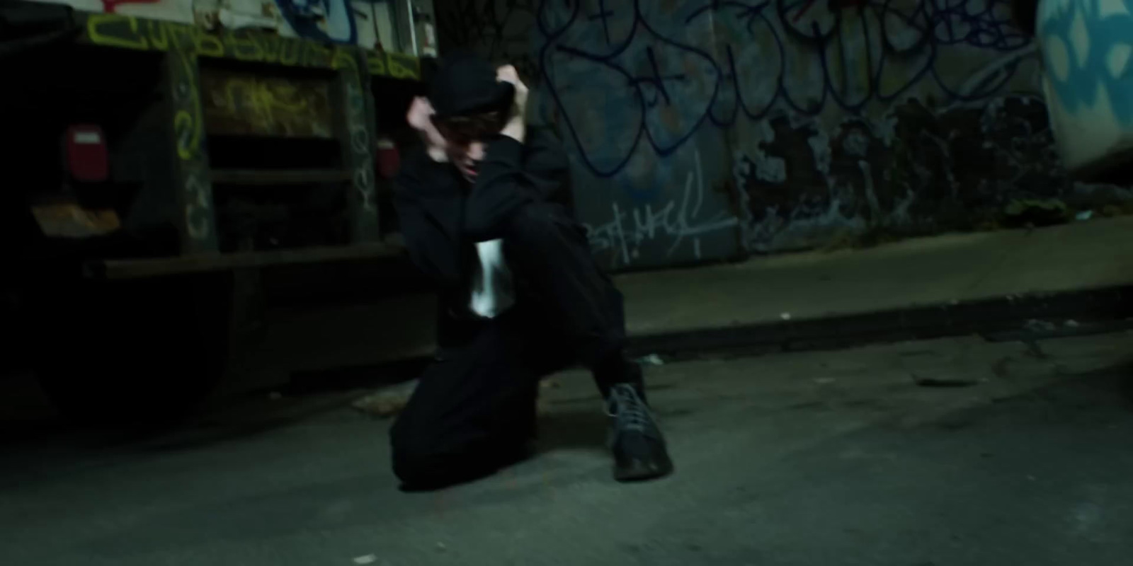 a man in a black suit and hat crouching on the ground