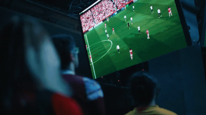 a group of people watching a soccer game on a big screen