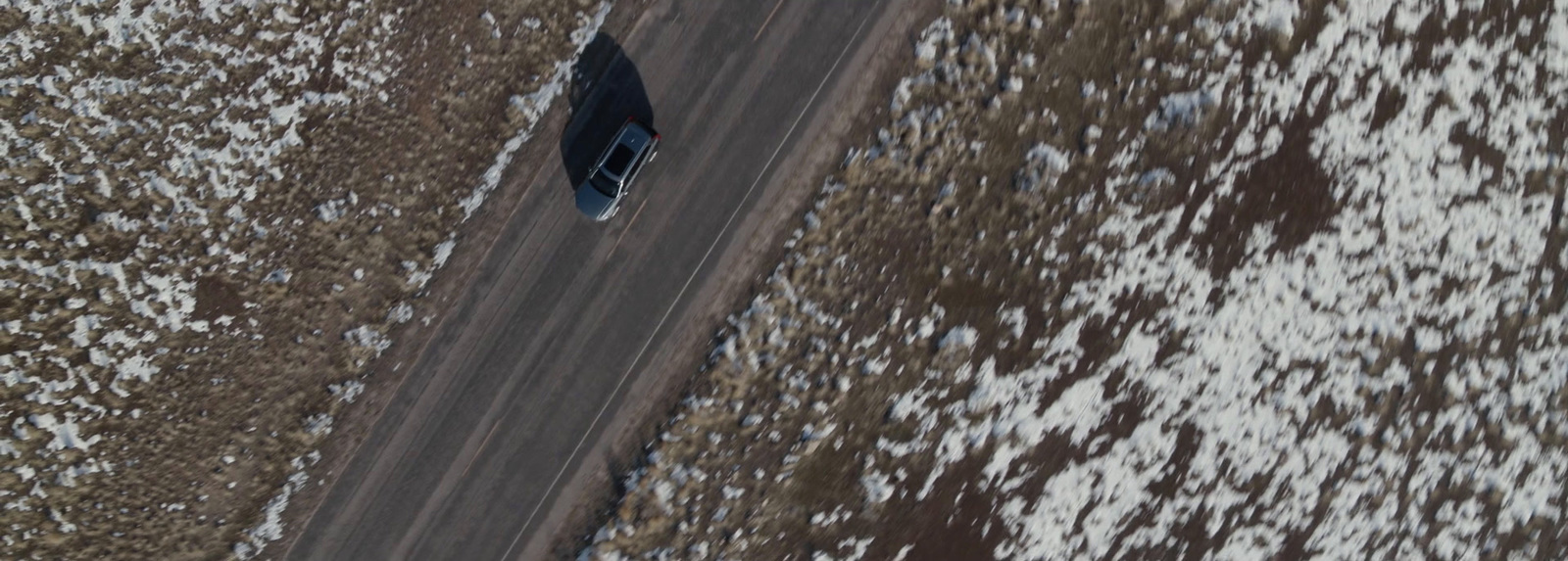 an aerial view of a car driving down a snowy road