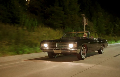 a black car driving down a street at night