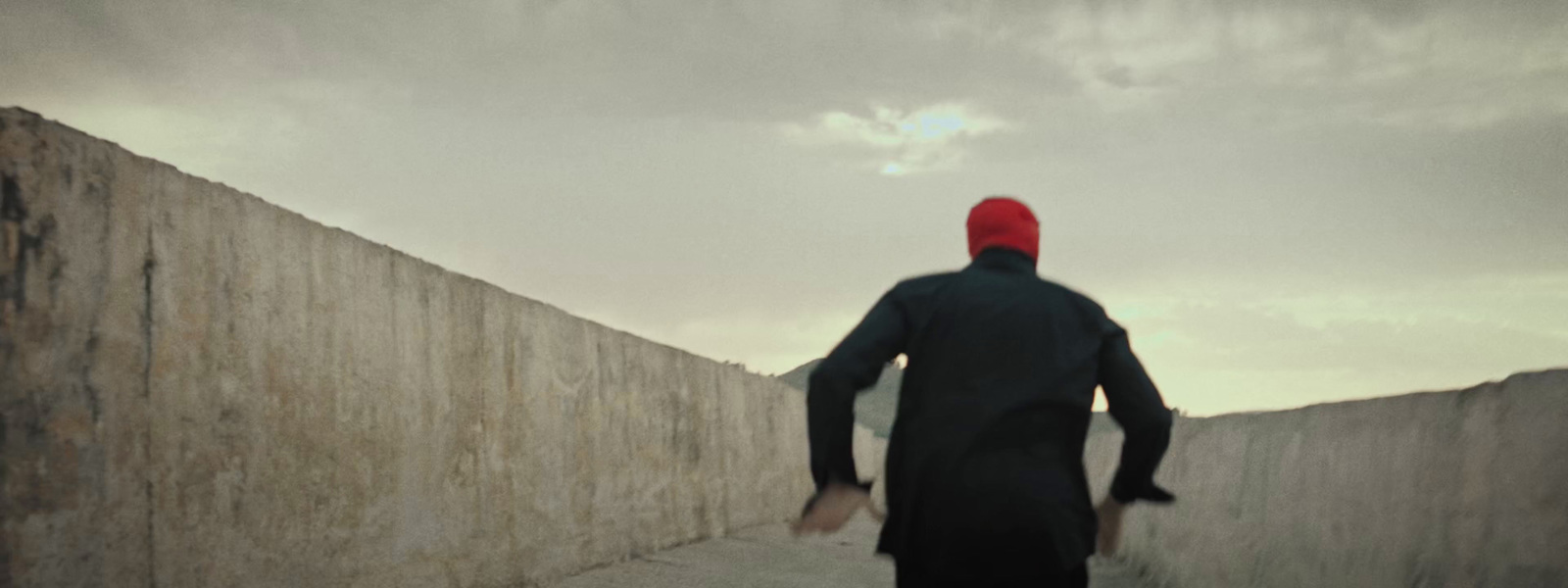 a man in a black coat and a red hat walking up a wall