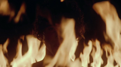 a man with long hair standing in front of a fire