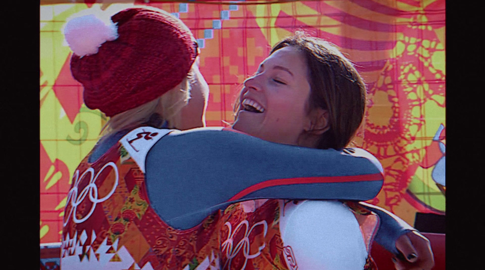 a woman is hugging another woman in front of a colorful wall