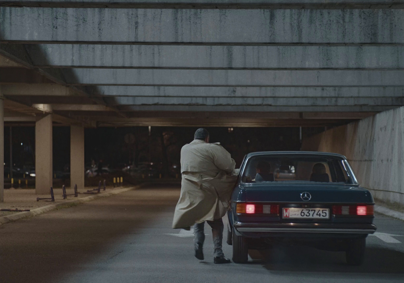 a man in a trench coat walking towards a car