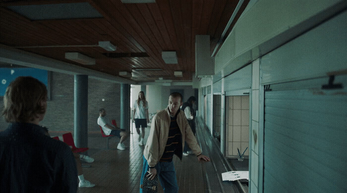 a man walking down a hallway carrying a skateboard