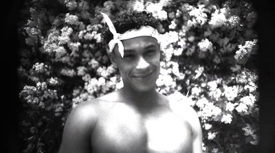 a shirtless man standing in front of a bush of flowers