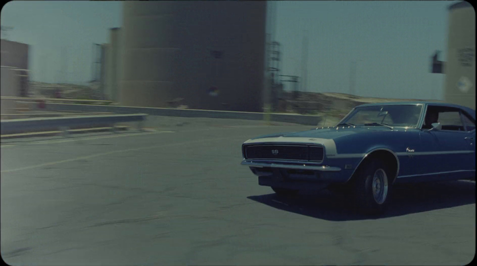 a blue car driving down a street next to tall buildings