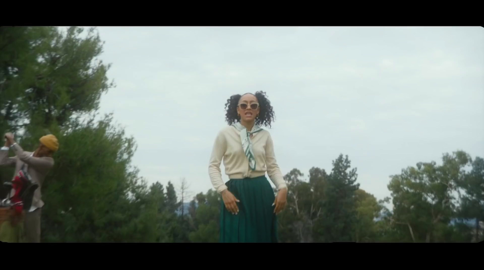 a woman in a long green skirt standing in front of trees