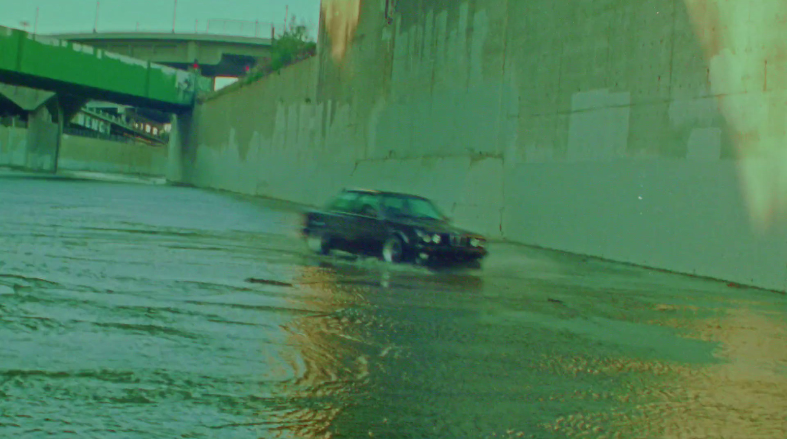 a car driving through a flooded street next to a bridge