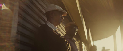 a man in a suit and hat leaning against a building