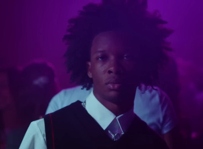 a man with dreadlocks standing in front of a purple background