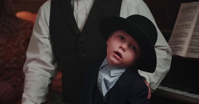 a young boy in a suit and hat standing in front of a piano