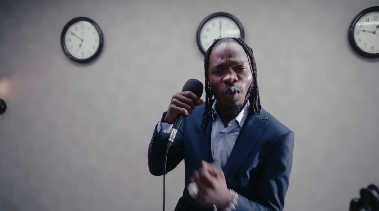 a man holding a microphone in front of three clocks