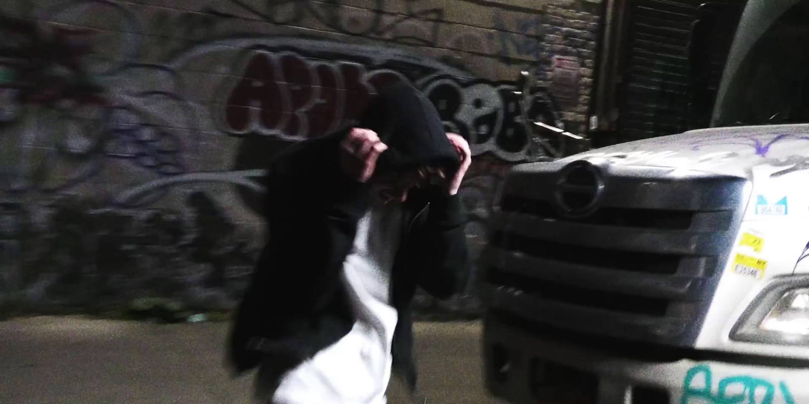 a man walking past a parked truck in front of a graffiti covered wall