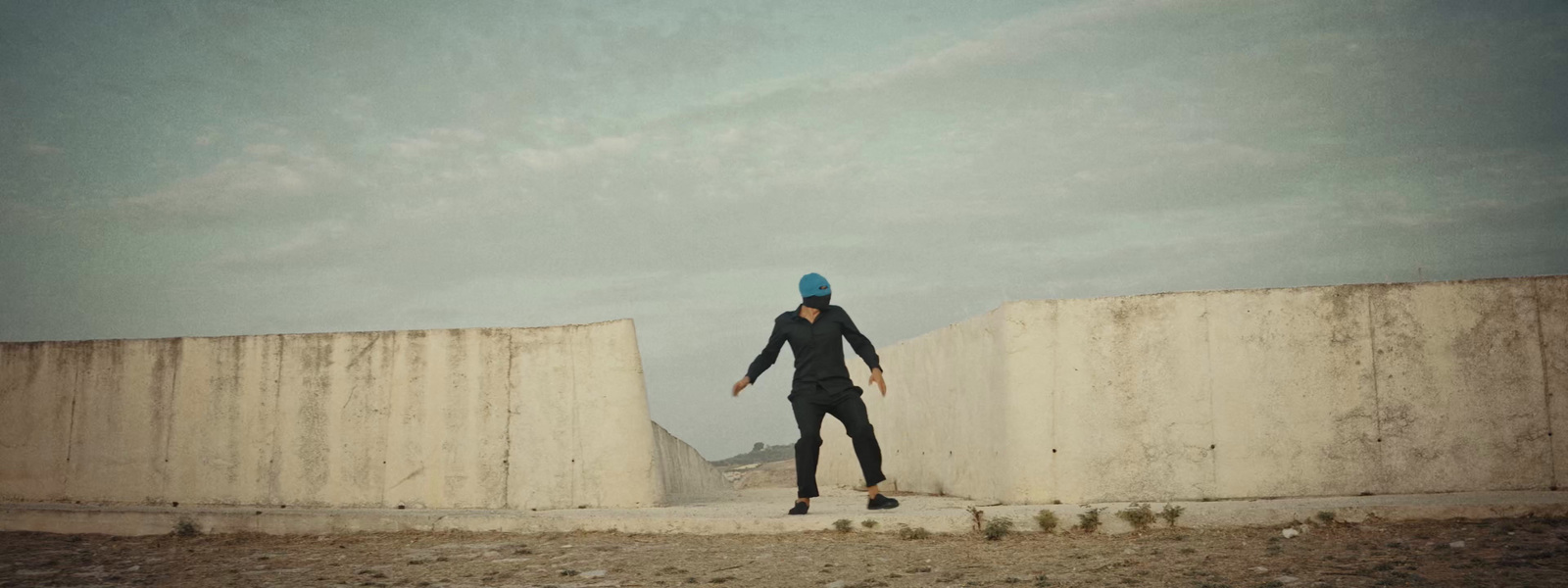 a man in a blue hat standing next to a cement wall