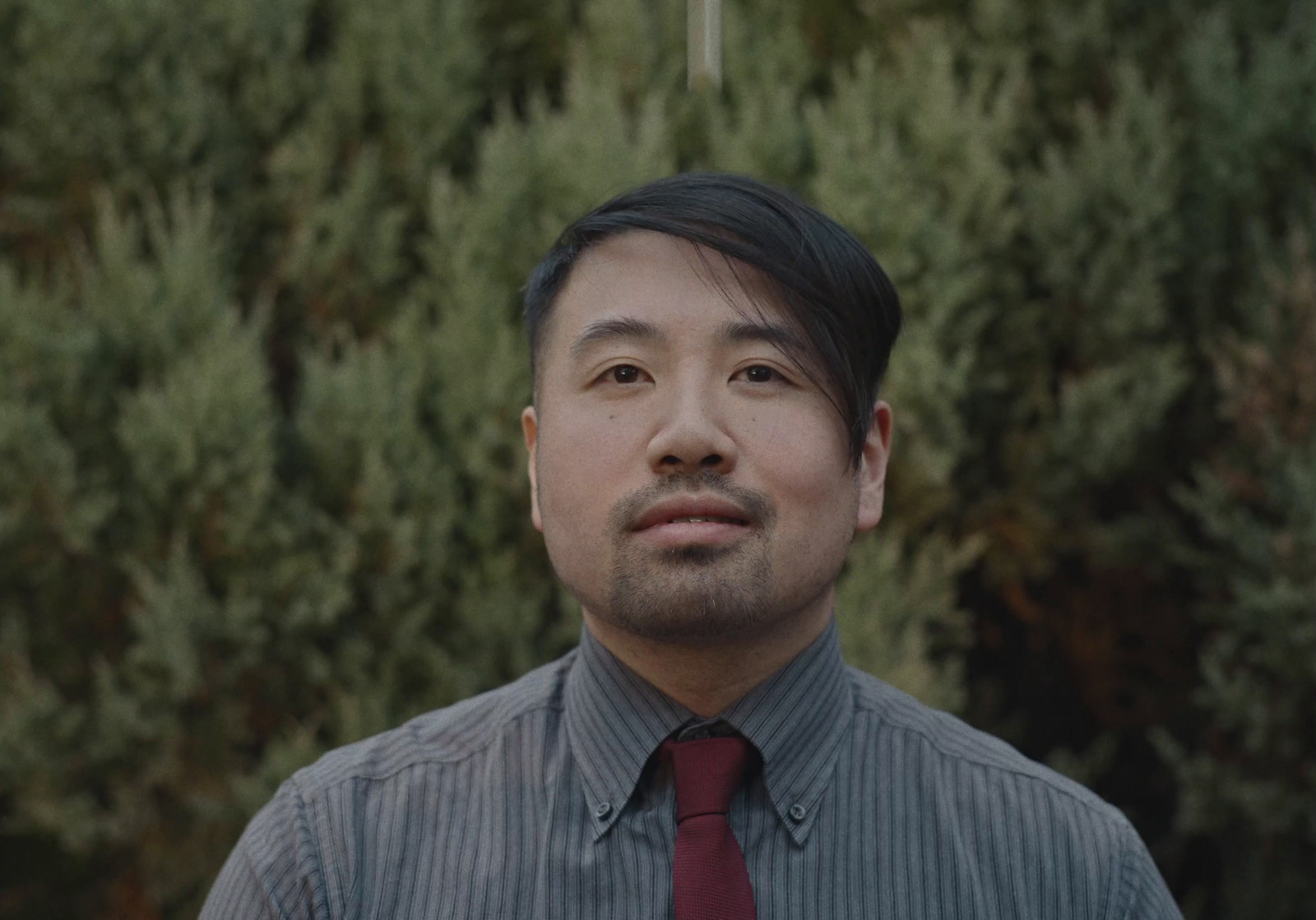 a man with a tie standing in front of some trees