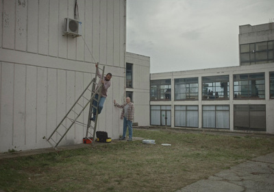 two people standing on a ladder in front of a building