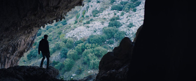 a man standing in a cave looking out at the mountains